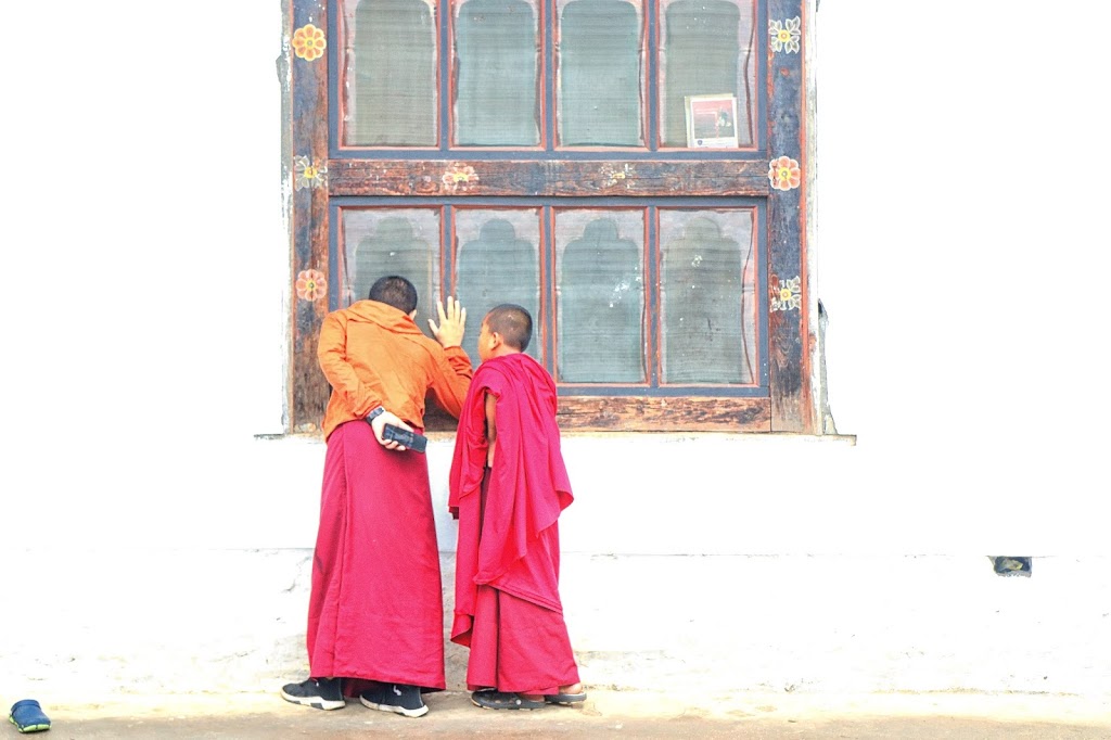 Image of two young monks looking through the window of a residential hall in Khuruthang Monastery, Punakha. 