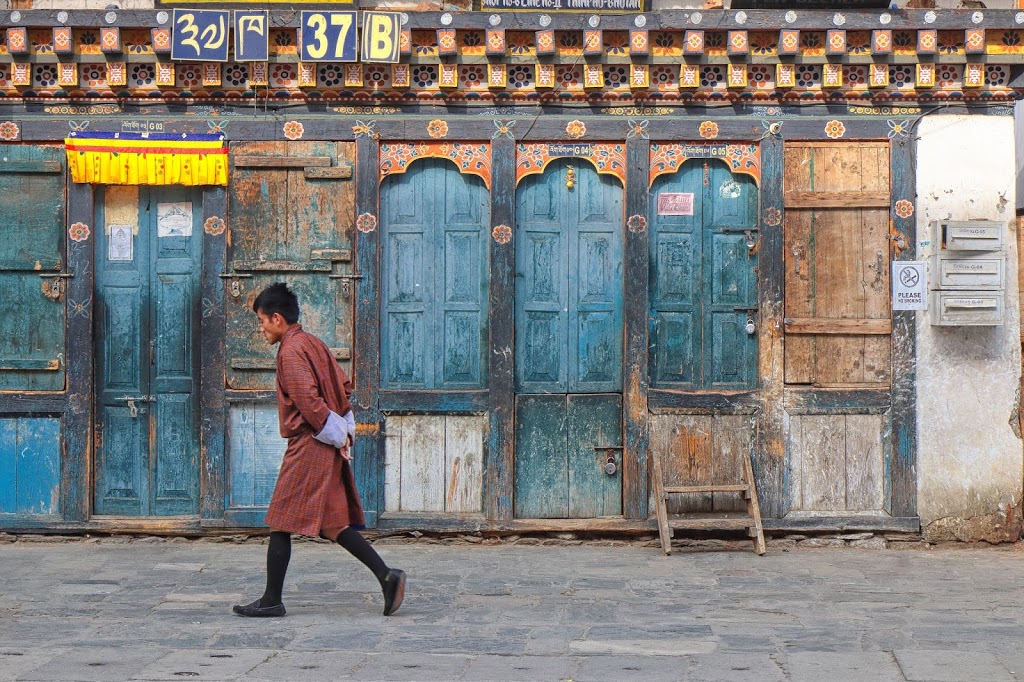Image of a Bhutanese man walking past a closed shop in Thimphu, wearing traditional dress Gho 