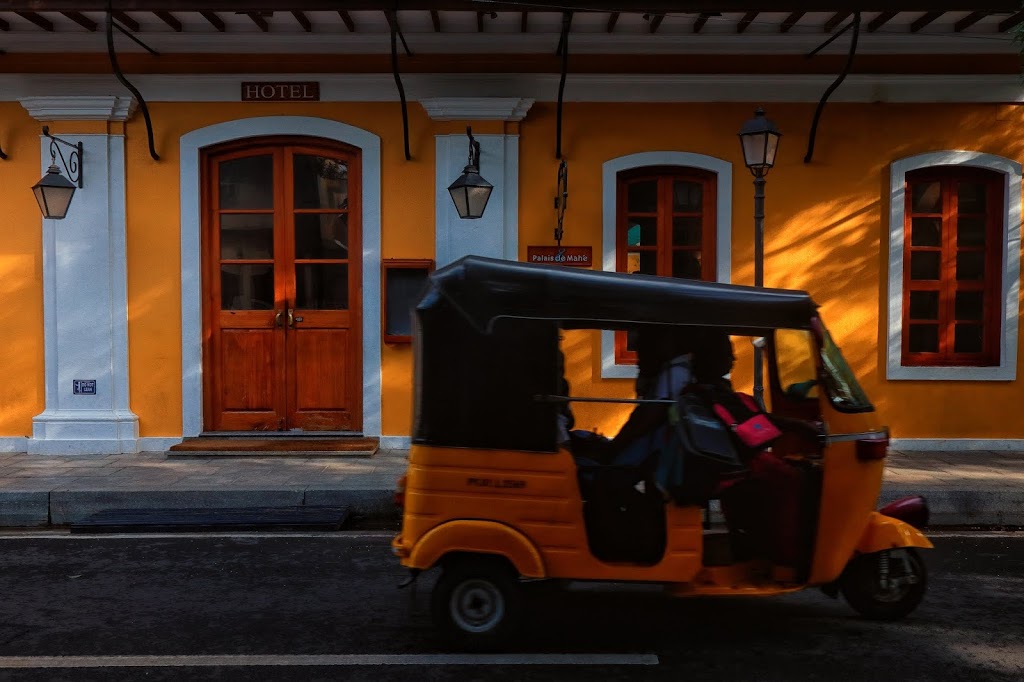 A yellow and black auto-rickshaw passing in front of the yellow walls of Palais De Mahe, an luxury hotel in White Town in Pondicherry.